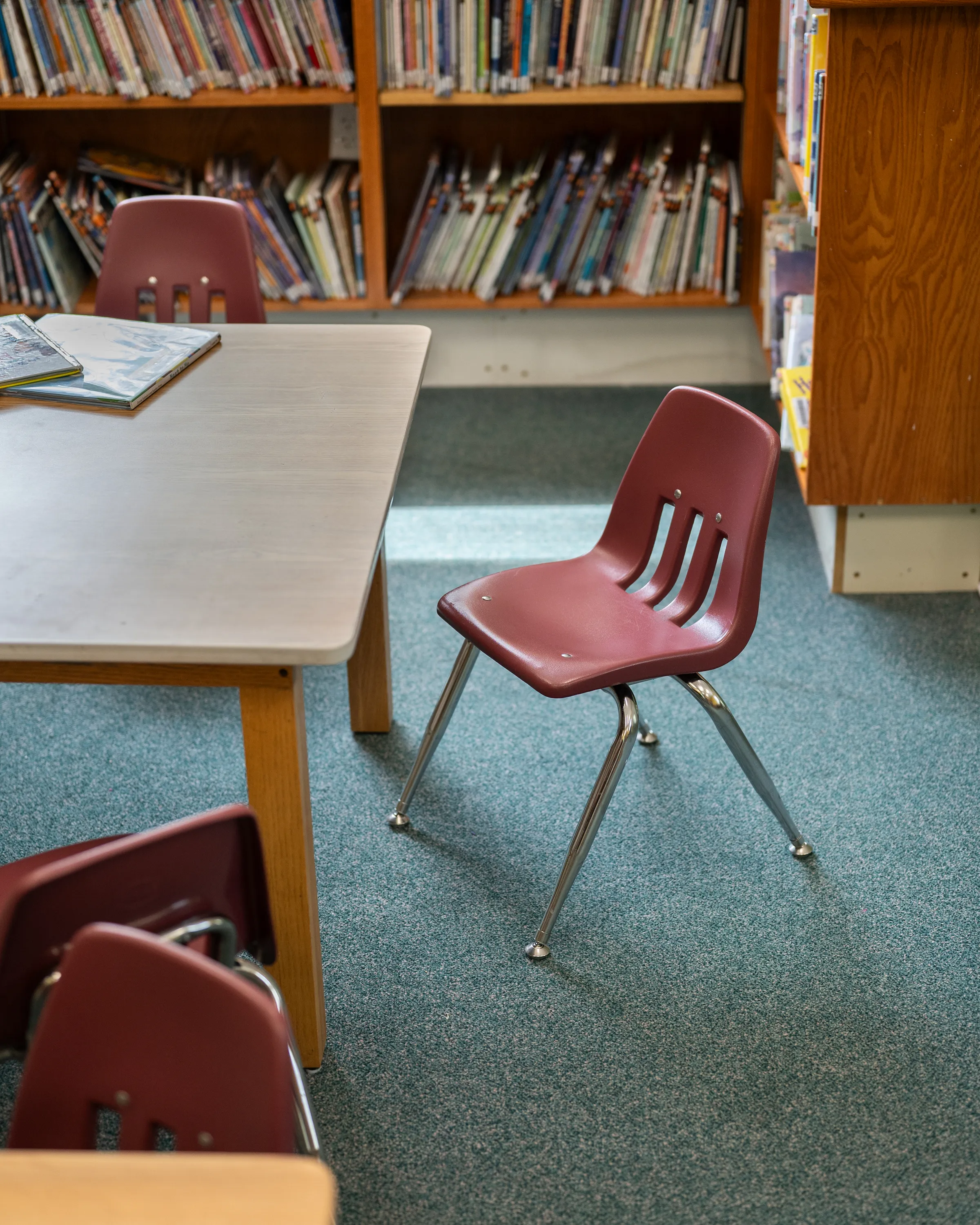 A child-sized chair beside a low table in the library's children's area, with shelves of picture books behind it