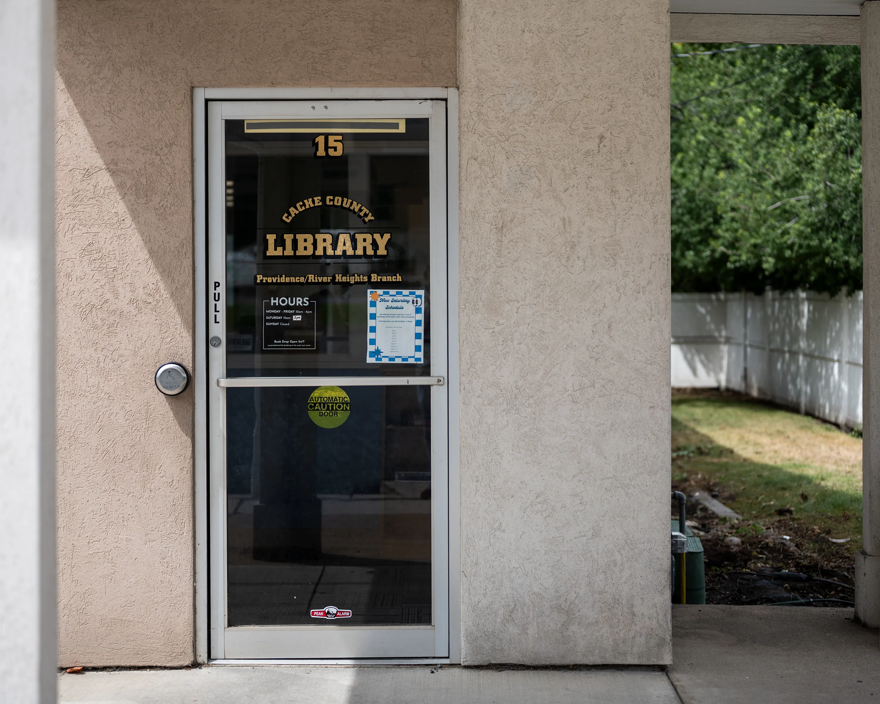 The library's glass front door under its covered entrance, lettered with Cache County Library, Providence/River Heights Branch, with hours posted